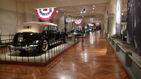1993 Ford Taurus - A vintage black convertible with a tan top is displayed in a museum hallway with other vehicles.