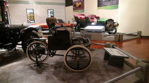 1993 Ford Taurus - An antique black automobile with large spoked wheels and a tall seat is displayed in a museum alongside other vintage vehicles.
