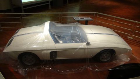 1993 Ford Taurus - A white concept car is covered in plastic sheeting, displayed indoors.