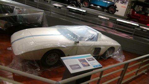 1993 Ford Taurus - A white concept car is covered in plastic at a museum exhibit, with other vehicles visible in the background.