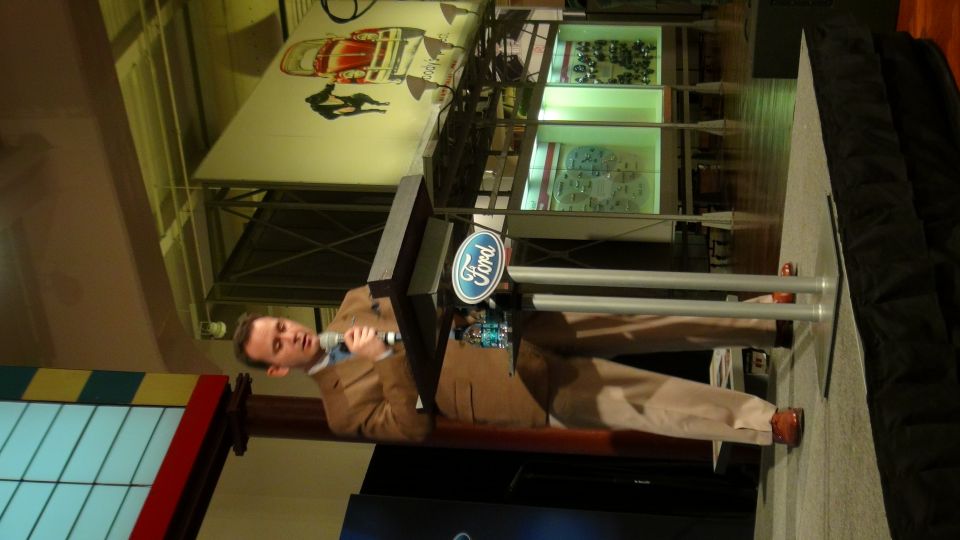 Ford logo on display stand with a man speaking into a microphone