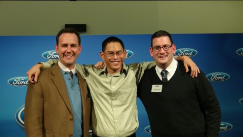 1993 Ford Taurus - Three men smile for a photo in front of a backdrop multiple Ford logos.
