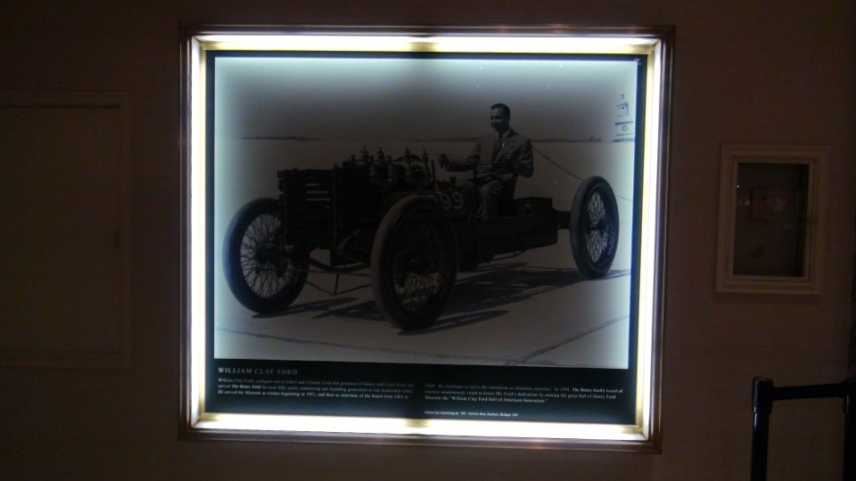 Black and white photo of William Clay Ford driving a vintage race car with large spoked wheels and an exposed engine
