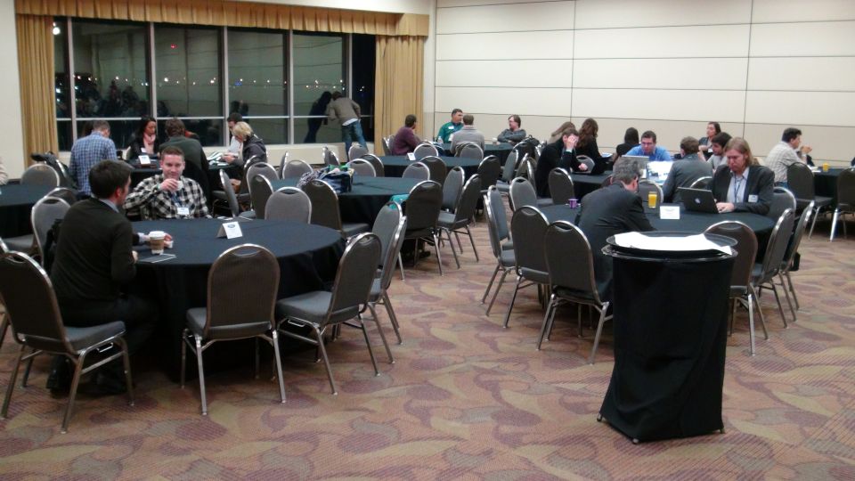 Conference room with round tables covered in black cloths, chairs around them, and people seated and standing