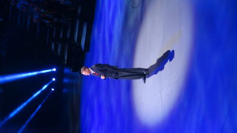 1993 Ford Taurus - A man in a suit stands on a stage illuminated by blue lights and spotlights.