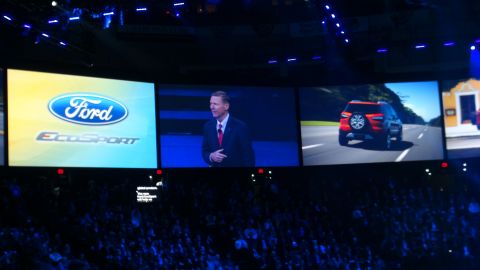 1993 Ford Taurus - A red Ford EcoSport is shown driving on a road, displayed on a large screen at an event.