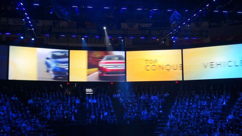 Large screen displays show a blue SUV and a red car, with text 'TOP CONQUE' and 'VEHICLE'