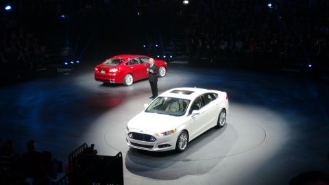 1993 Ford Taurus - A white Ford sedan is presented on stage, with a red Ford sedan and a presenter in the background.