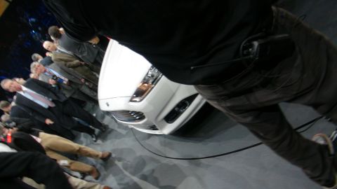 1993 Ford Taurus - A white car is displayed at an auto show with attendees gathered around.