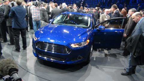 1993 Ford Taurus - A blue Ford sedan is displayed with its door open, surrounded by onlookers at an auto show.