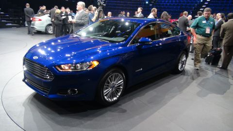 1993 Ford Taurus - A blue sedan with hybrid badging is displayed at an auto show, with other vehicles and attendees in the background.