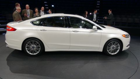 1993 Ford Taurus - A white sedan is displayed on a circular platform with several people observing.