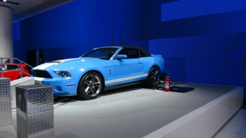 1993 Ford Taurus - A blue Ford Mustang GT500 convertible with racing stripes is displayed on a platform with a red fire extinguisher nearby.