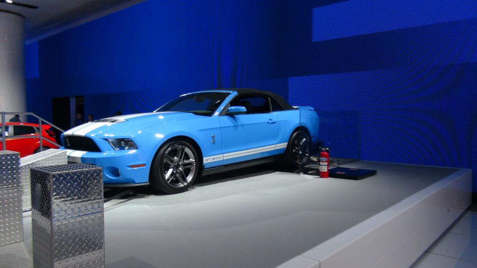 Blue convertible Ford Mustang GT500 with white stripes, black soft top, and chrome wheels on display