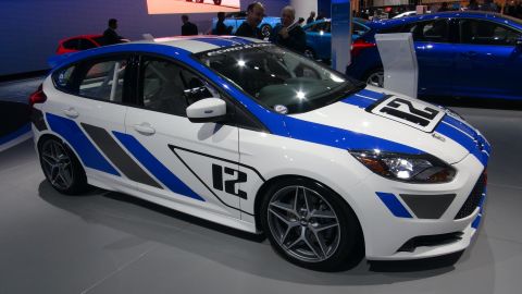 1993 Ford Taurus - A white Ford Focus with racing stripes and the number 12 is displayed at an auto show.