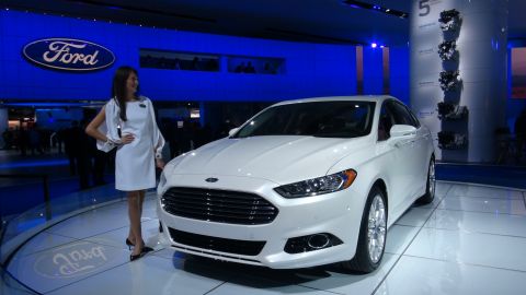1993 Ford Taurus - White Ford sedan displayed at an auto show with a promotional model.