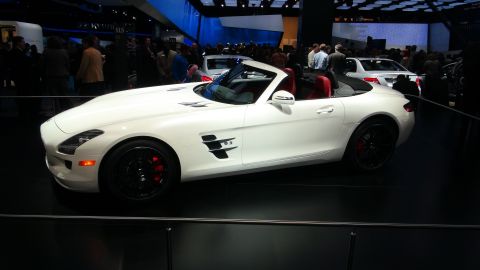 1993 Ford Taurus - A white convertible sports car is showcased at an auto show with other vehicles and attendees visible.
