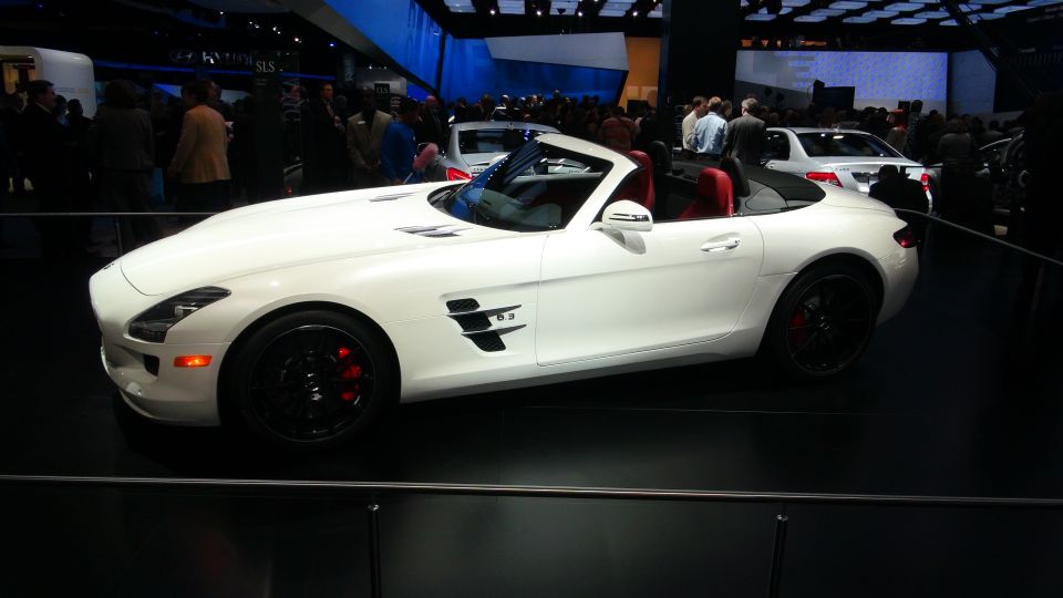 White convertible sports car with red interior on display, other cars and people in background