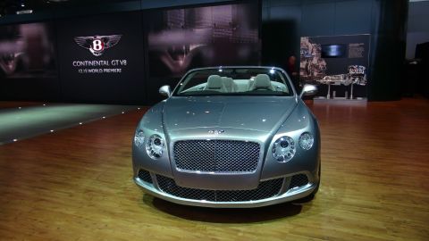 1993 Ford Taurus - A silver Bentley Continental GT V8 convertible is showcased at an auto show with a display behind it.