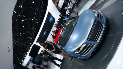 1993 Ford Taurus - A blue sports car is displayed at an auto show with other vehicles and people around.