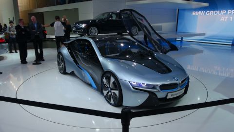 1993 Ford Taurus - A futuristic BMW i8 is showcased at an auto show with its doors open, and a black sedan is visible in the background.