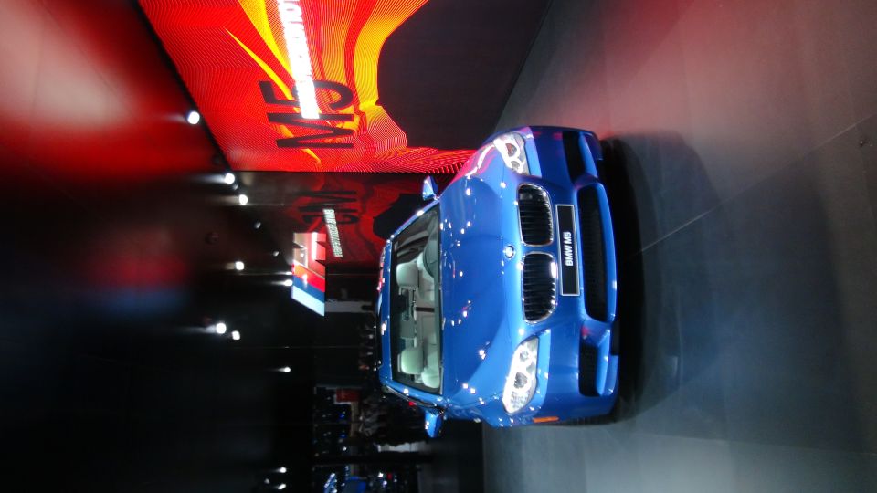 Blue BMW M5 with racing stripes on display at an auto show