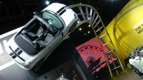 1993 Ford Taurus - A white convertible with black racing stripes is displayed at an auto show, with a large Ferris wheel graphic behind it.