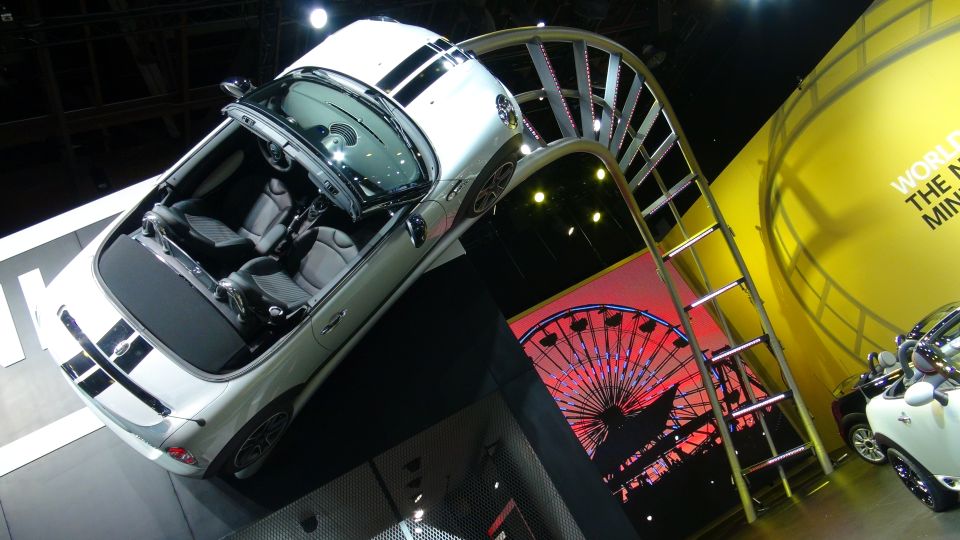 White convertible with black stripes on display with a Ferris wheel backdrop