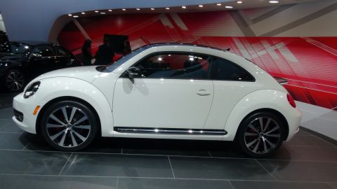 1993 Ford Taurus - Side view of a white Volkswagen Beetle on display at an auto show with a black car in the background.