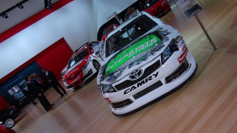 1993 Ford Taurus - A white Toyota Camry race car with green Interstate Batteries livery is displayed at an auto show alongside other vehicles.