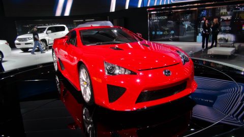 1993 Ford Taurus - A red Lexus sports car is showcased at an auto show, with a white SUV visible behind it.