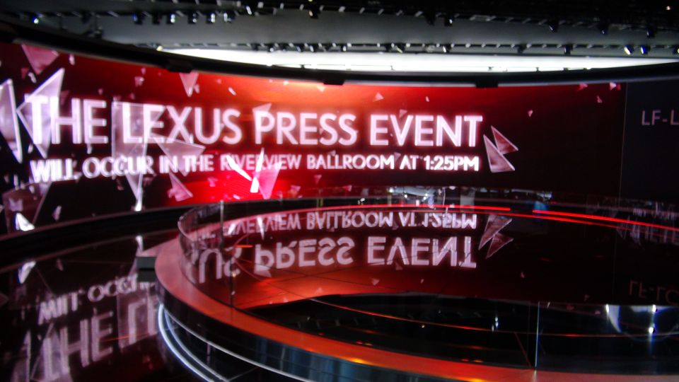 Digital display announcing 'THE LEXUS PRESS EVENT WILL OCCUR IN THE RIVERVIEW BALLROOM AT 1:25PM' with reflections