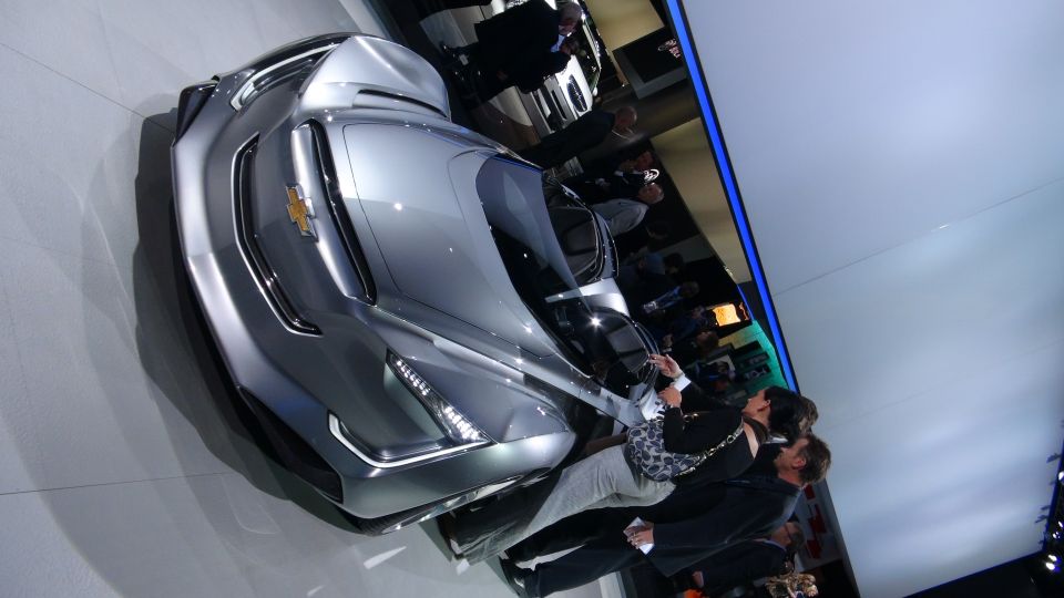 Silver Chevrolet concept car with gold bowtie emblem, viewed from a 3/4 front angle at an auto show