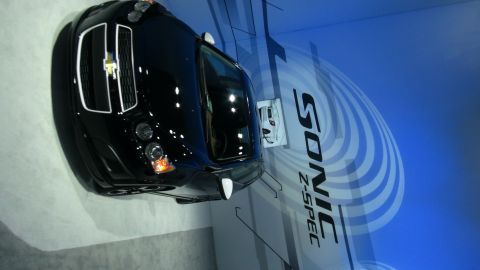 1993 Ford Taurus - A black Chevrolet Sonic Z-Spec is displayed with prominent branding in the background.