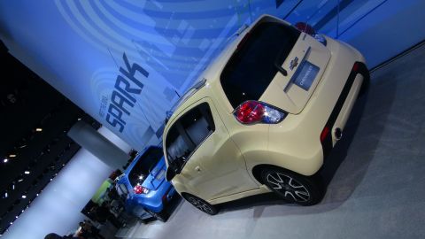 1993 Ford Taurus - Cream and blue Chevrolet Spark models are displayed at an auto show with "SPARK" branding in the background.