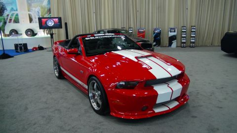 1993 Ford Taurus - A red convertible sports car with racing stripes is displayed indoors, with other vehicles and displays in the background.