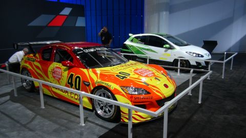 1993 Ford Taurus - Two cars on display at an auto show, one a race car and the other a hatchback.