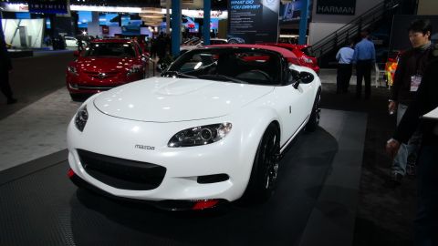 1993 Ford Taurus - A white Mazda convertible is displayed at an auto show, with a red car in the background.