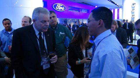 1993 Ford Taurus - Attendees converse at a Ford event, with the company's prominent logo visible in the background.
