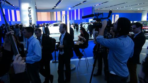 1993 Ford Taurus - Media personnel film at an auto show, with several vehicles displayed in the background.