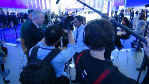1993 Ford Taurus - A media crew films attendees at an auto show, with a white car visible in the background.