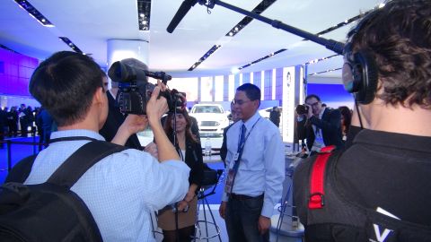1993 Ford Taurus - Press event at an auto show with media filming attendees and a car display.