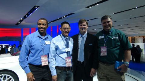 1993 Ford Taurus - Four men pose for a photo at an auto show, with a white vehicle partially visible in the foreground.