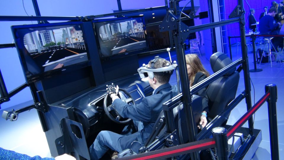 Car simulator with two people inside, one wearing a VR headset and steering