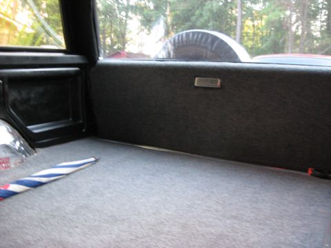 1988 Ford Bronco - The rear cargo area of a 1988 Ford Bronco features grey carpeting and a spare tire mounted externally, visible through the rear window.