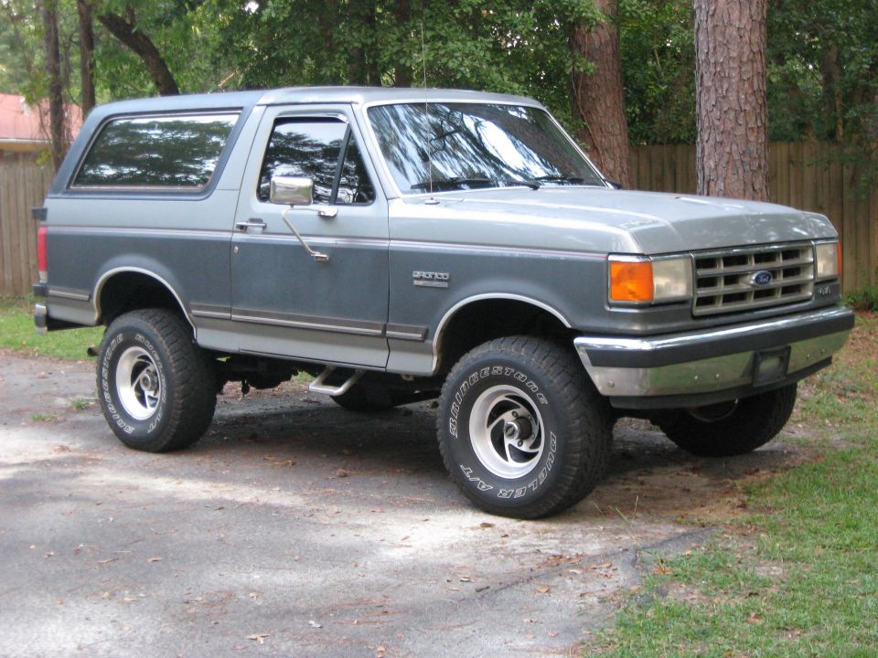 Two-tone gray 1988 Ford Bronco with aftermarket wheels parked on a gravel driveway