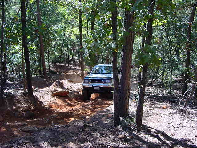 White 4x4 pickup working down a rocky shaded dirt trail through hardwood timber