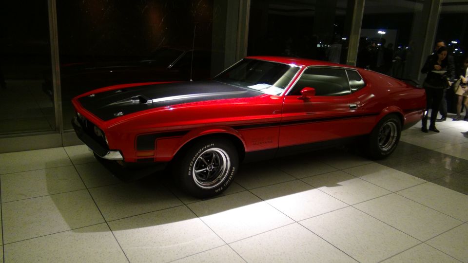 Red 1971 Ford Mustang Mach 1 with black hood stripe and side stripe, parked indoors