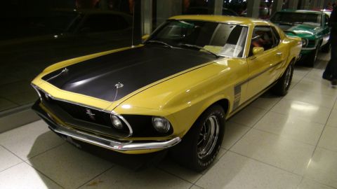 1993 Ford Taurus - A yellow 1969 Ford Mustang Boss 302 is parked next to another vehicle inside a building.