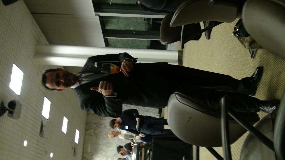 Man in suit holding a drink, gesturing with thumb up and pointing